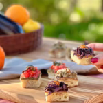Crostini colorati su tagliere con verdure di stagione e mano femminile | Colorful crostini on a wooden board with seasonal vegetables and a woman's hand